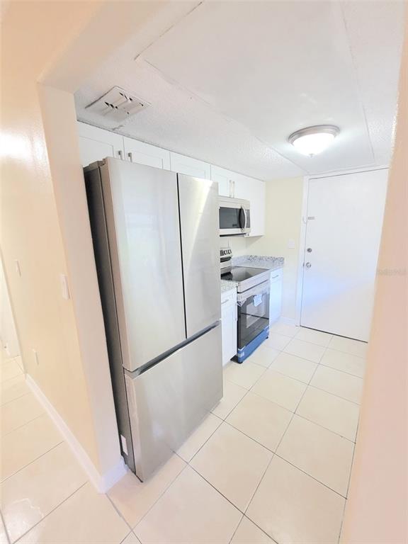 A kitchen features stainless steel appliances, white cabinetry, and light-colored tile flooring — 5338 ORANGE AVENUE UNIT B, SEFFNER, FL