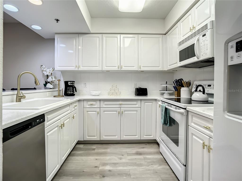 A kitchen features white cabinetry, stainless steel appliances, a gold faucet, and light wood flooring — 5300 S ATLANTIC AVENUE UNIT 10-205, NEW SMYRNA BEACH, FL