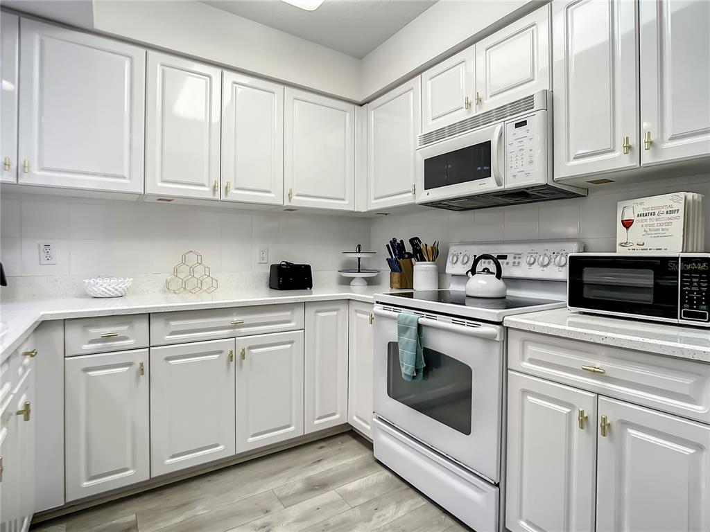 A white kitchen features white cabinets, light countertops, stainless steel appliances, and wood-look flooring — 5300 S ATLANTIC AVENUE UNIT 10-205, NEW SMYRNA BEACH, FL