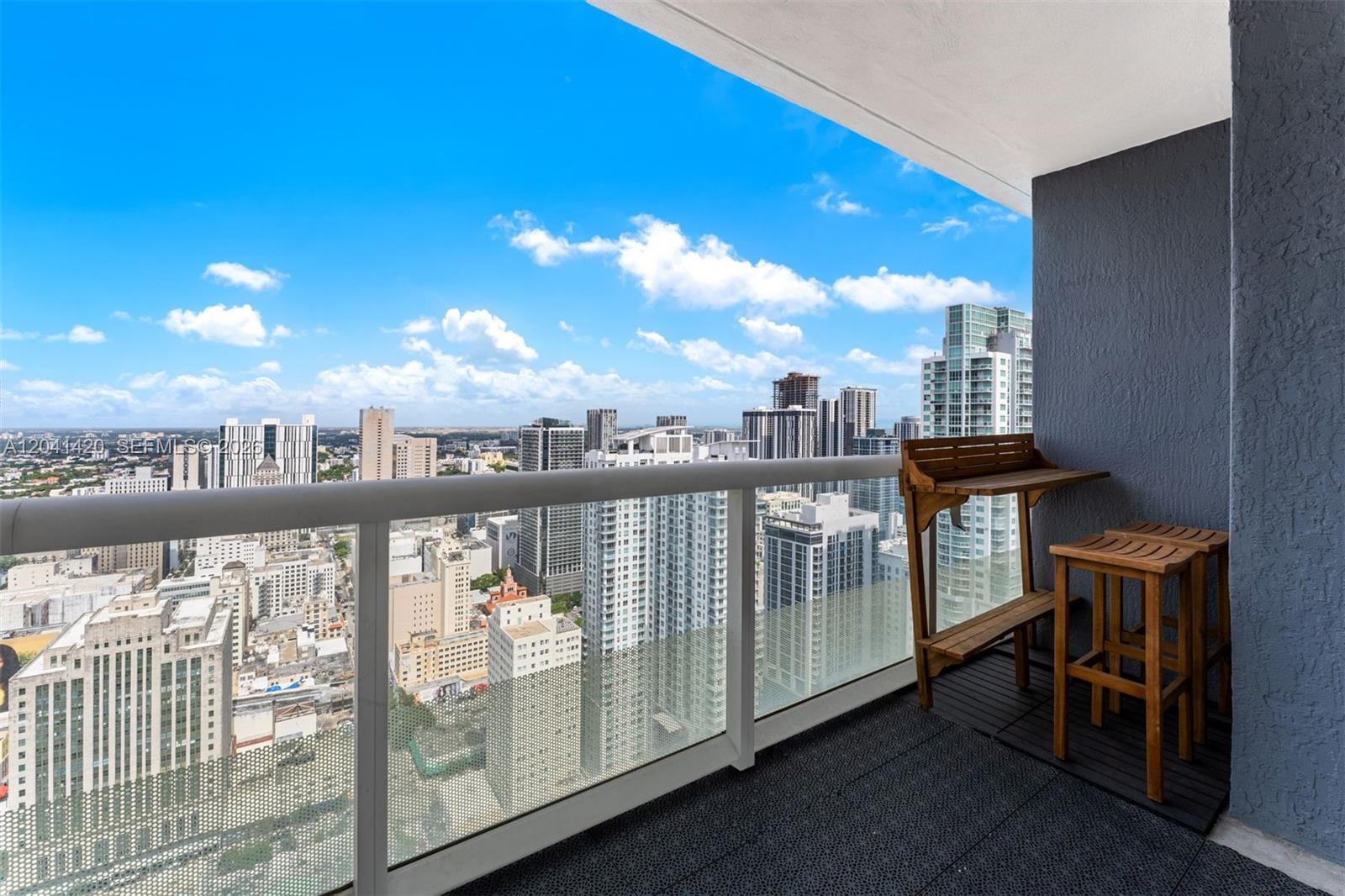 A high-rise balcony features a wooden bar table with stools overlooking a dense city skyline — 50 Biscayne Blvd # 4603, Miami FL 33132, MIAMI, FL