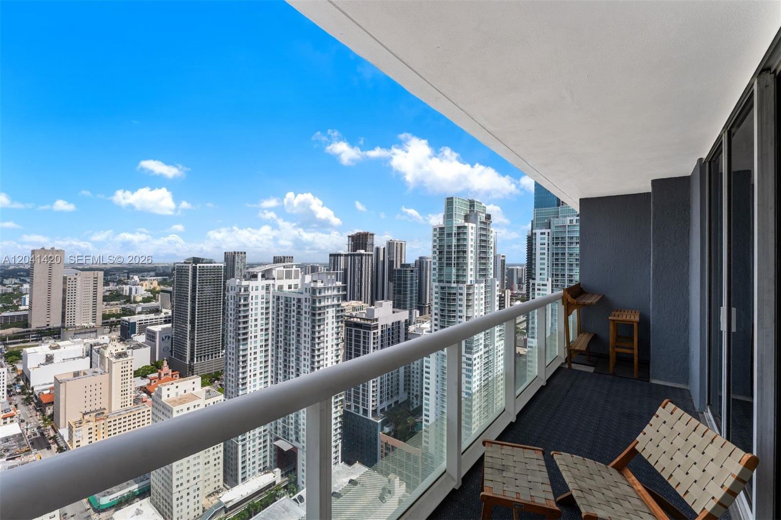 A high-rise balcony with a glass railing overlooks a dense city skyline under blue skies — 50 Biscayne Blvd # 4603, Miami FL 33132, MIAMI, FL