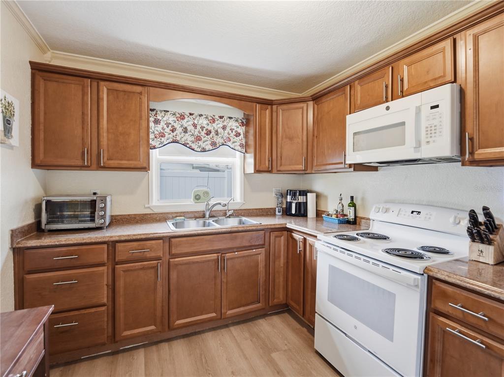 A kitchen features wood cabinets, laminate countertops, white appliances, and a window above the sink — 332 ILLINOIS AVENUE, ST CLOUD, FL