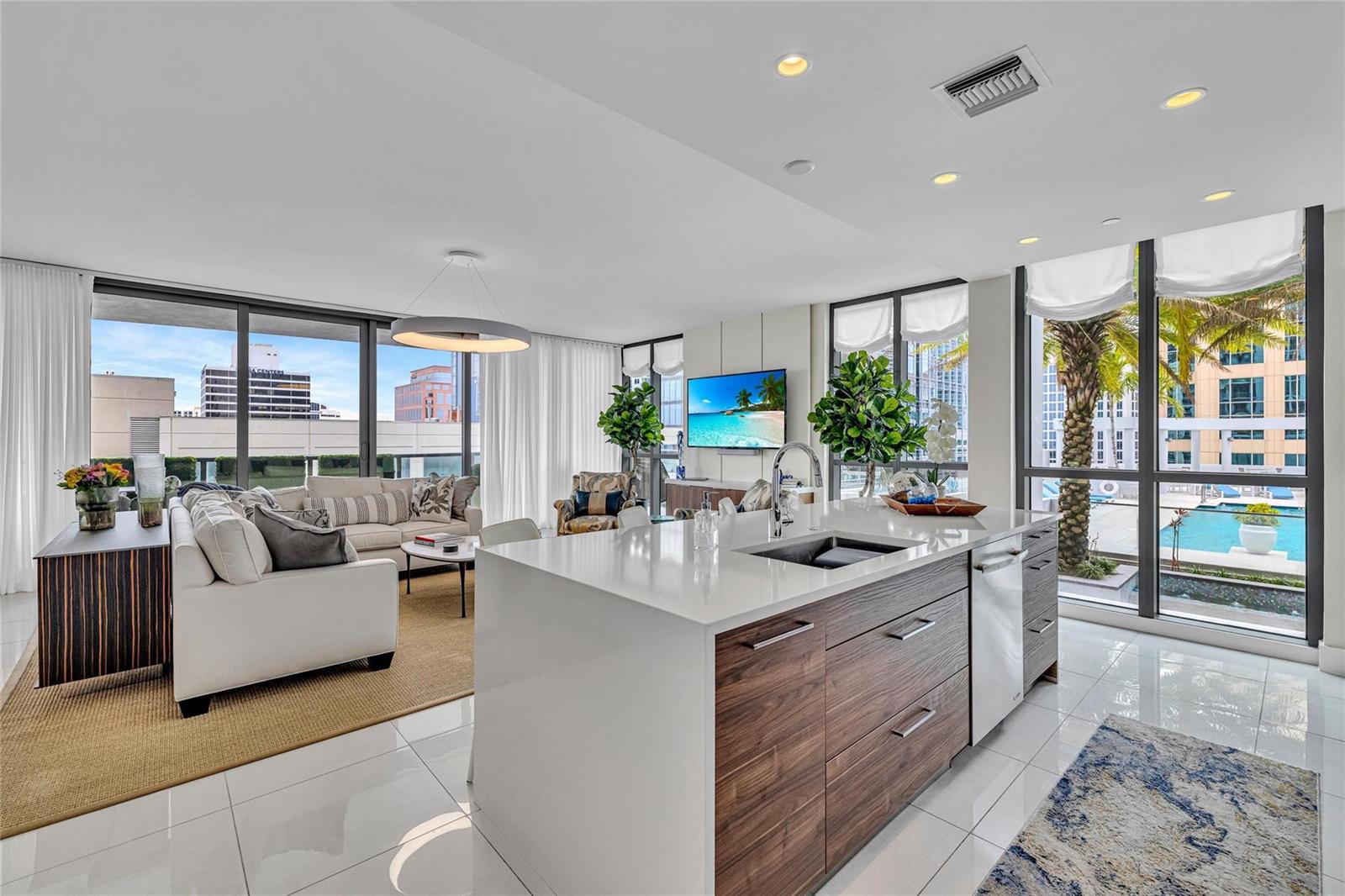 A modern kitchen island with wood cabinets and white countertops overlooks a living area — 100 E Las Olas Boulevard # 1701, Fort Lauderdale FL 33301, FORT LAUDERDALE, FL