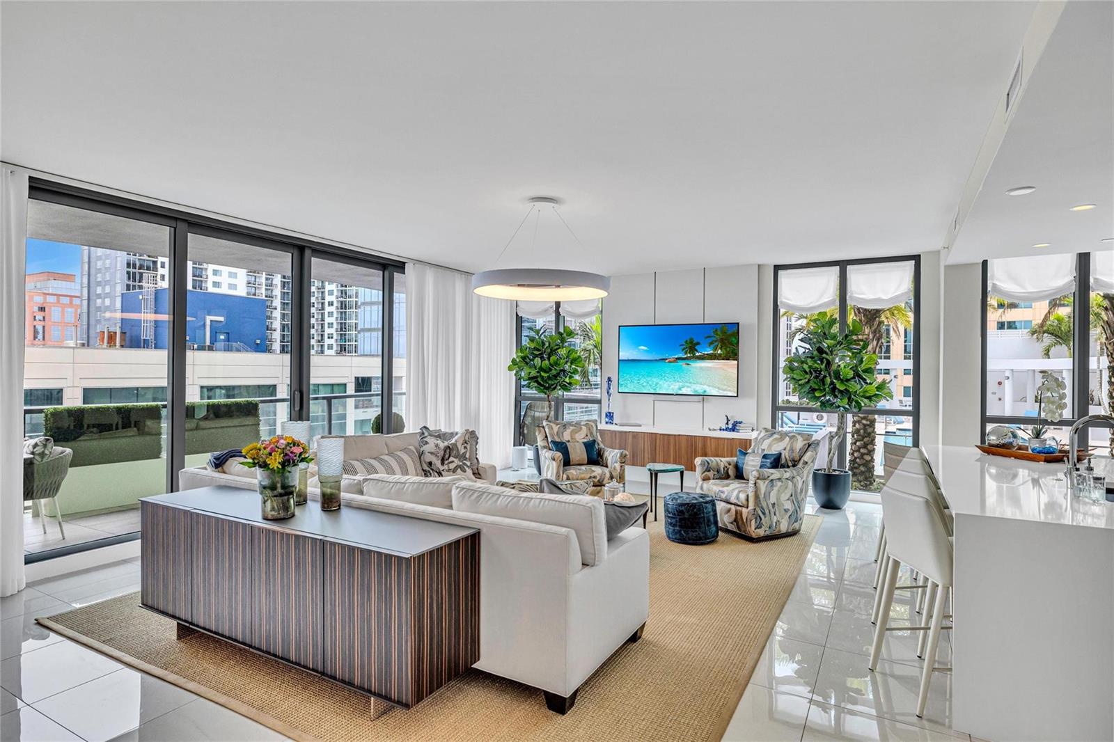 A modern living room features a white sofa, patterned armchairs, and a large wall-mounted television — 100 E Las Olas Boulevard # 1701, Fort Lauderdale FL 33301, FORT LAUDERDALE, FL