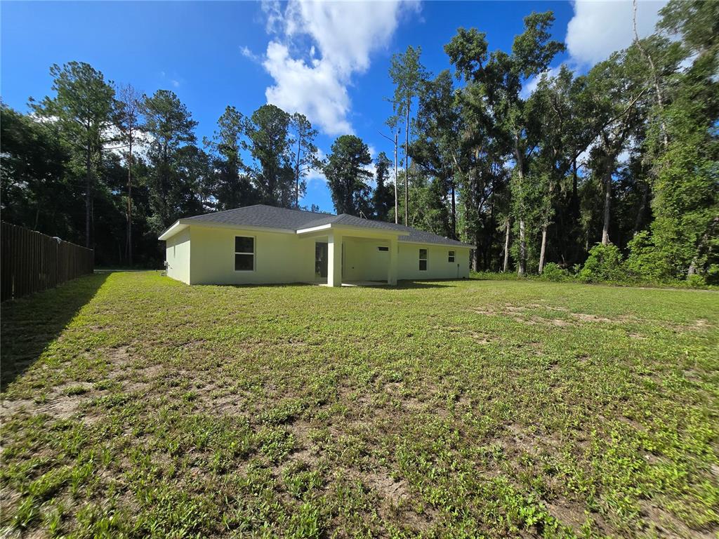 The rear exterior of a light-colored single-story house features a covered patio and yard — 11 SEQUOIA LOOP PLACE, OCKLAWAHA, FL