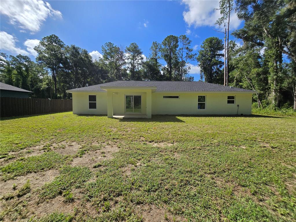 The rear exterior of a single-story house features a covered patio and a grassy yard — 11 SEQUOIA LOOP PLACE, OCKLAWAHA, FL