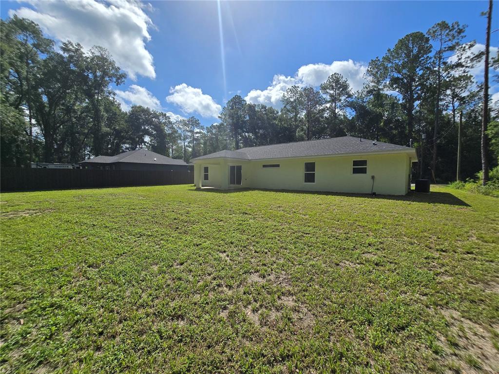 The back exterior of a light-colored house features a covered patio and a large yard — 11 SEQUOIA LOOP PLACE, OCKLAWAHA, FL