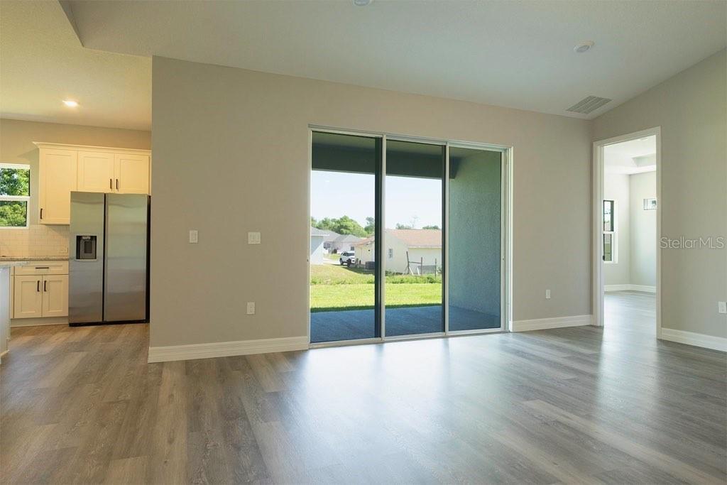 A living area with light-colored walls, wood-look flooring, and a sliding glass door to a patio — 2028 SW 153 LOOP, OCALA, FL