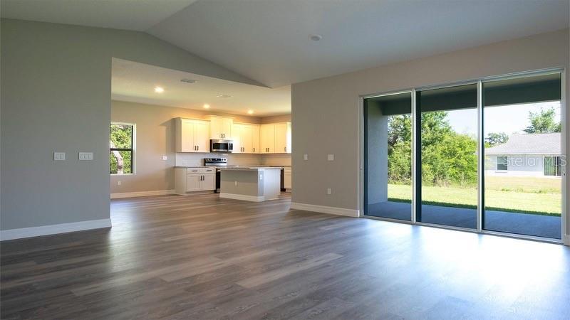 An open-concept living area features wood-look flooring, a kitchen with white cabinets, and sliding glass doors — 2028 SW 153 LOOP, OCALA, FL