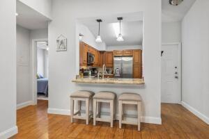 A kitchen with wooden cabinets and a breakfast bar with three stools faces a hallway — 3130 Millwood Terrace # 2110, Boca Raton FL 33431, BOCA RATON, FL