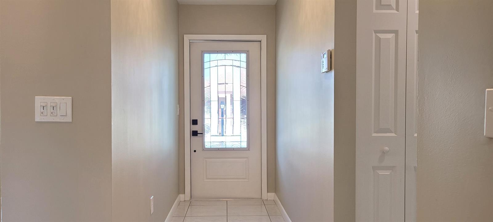 An entryway features a white front door with a glass insert and light-colored tile flooring — 6209 Olivewood Circle, FL 33463, FL