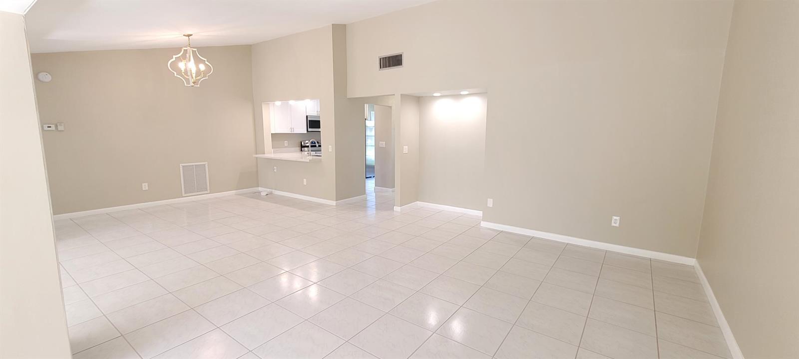 An open-concept living area features beige walls, white tile flooring, and a recessed kitchen pass-through — 6209 Olivewood Circle, FL 33463, FL