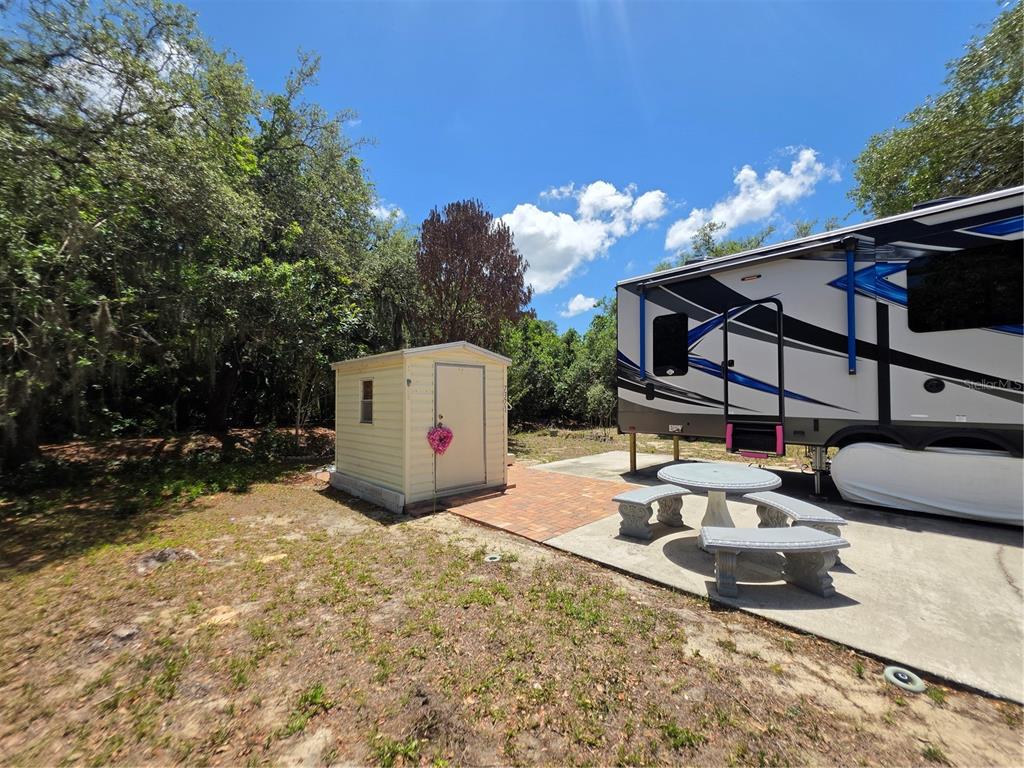 A beige storage shed sits on a brick patio next to a parked recreational vehicle — 7371 INTERNATIONAL CIRCLE, LAKE WALES, FL