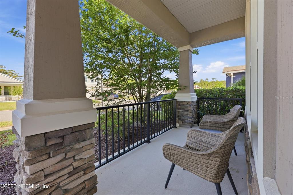 A covered front porch features stone-based columns, a black metal railing, and two wicker chairs — 6946 AZALEA GROVE DRIVE, JACKSONVILLE, FL