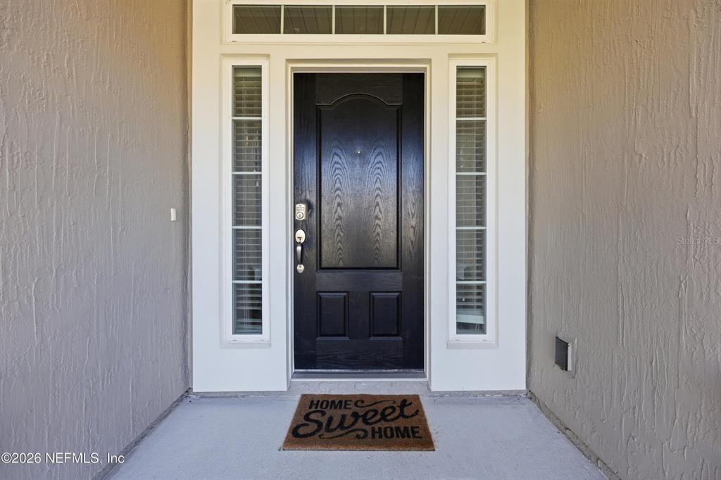 A black front door with sidelights and a transom window sits on a concrete porch — 6946 AZALEA GROVE DRIVE, JACKSONVILLE, FL