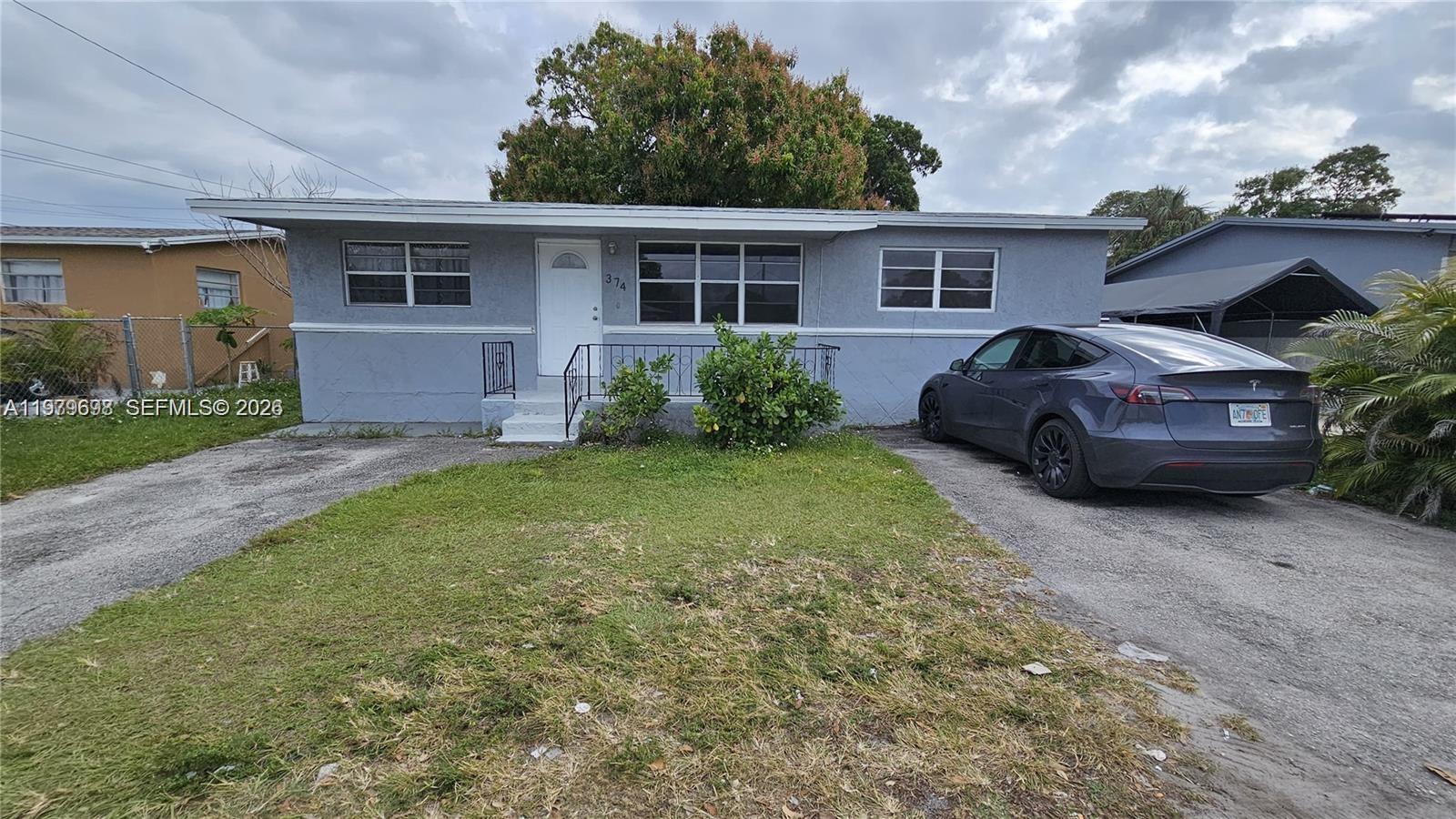A gray single-story house features a front lawn, a concrete driveway, and a parked car — 374 NW 31st Ave, Pompano Beach FL 33311, POMPANO BEACH, FL