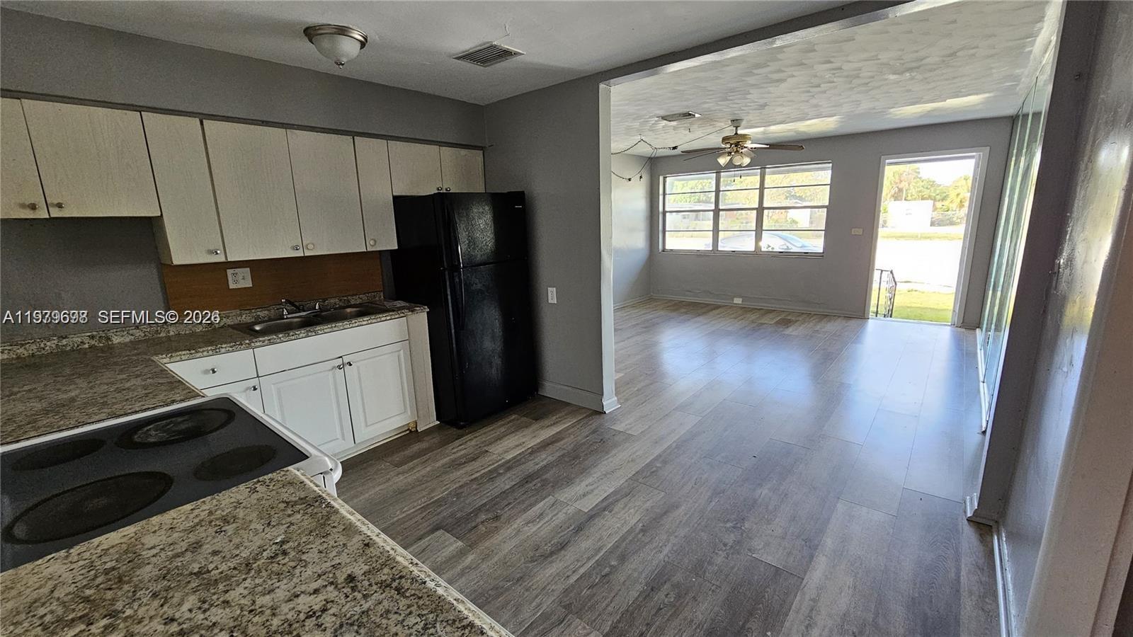 A kitchen with white cabinets and a black refrigerator opens into a living area — 374 NW 31st Ave, Pompano Beach FL 33311, POMPANO BEACH, FL