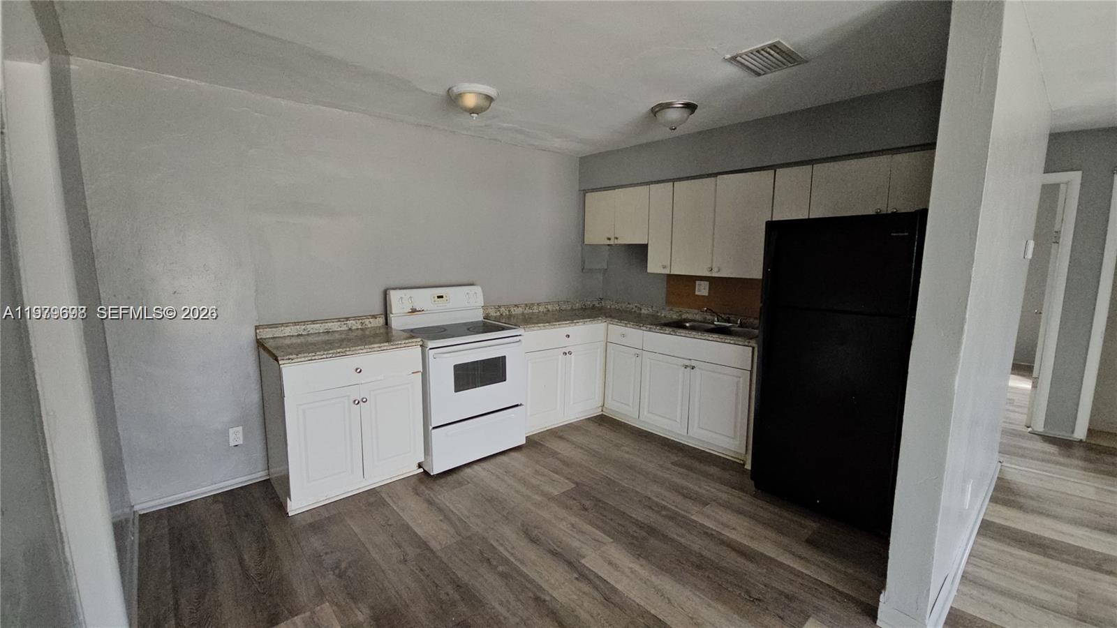A kitchen features white cabinets, a white stove, a black refrigerator, and wood-look flooring — 374 NW 31st Ave, Pompano Beach FL 33311, POMPANO BEACH, FL