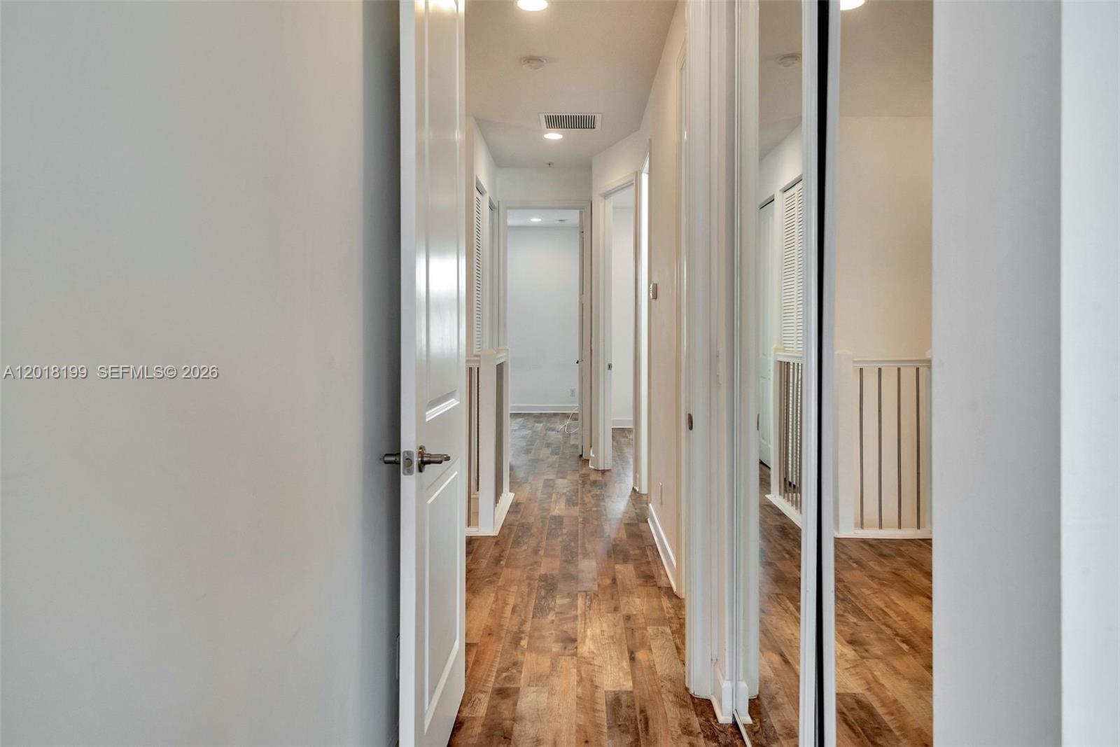 A hallway with wood-look flooring leads to an open doorway and a mirrored closet — 22954 Clear Echo Dr # 29, Boca Raton FL 33433, BOCA RATON, FL