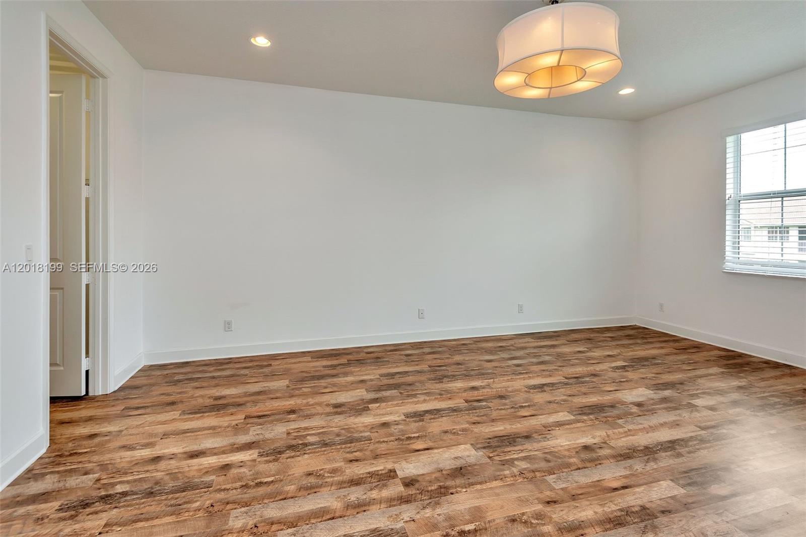 An empty room features white walls, wood-look flooring, a modern drum light, and a window — 22954 Clear Echo Dr # 29, Boca Raton FL 33433, BOCA RATON, FL