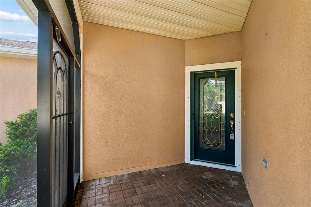A covered entryway features a dark green front door with decorative glass and brick flooring — 230 BAY DRIVE, KISSIMMEE, FL