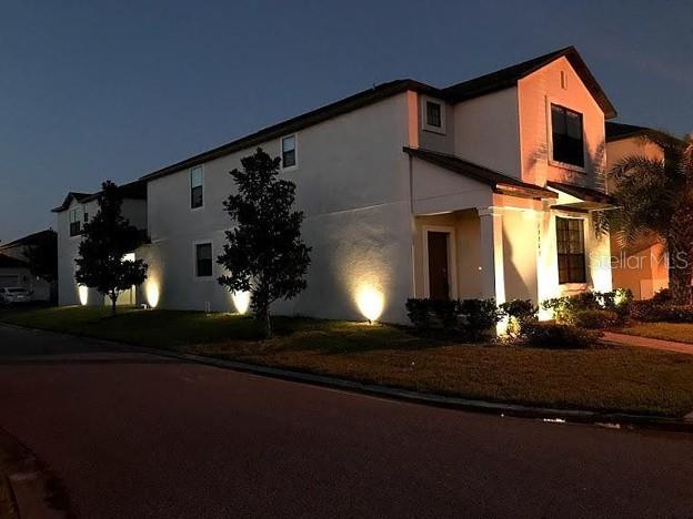 A two-story house with exterior lighting at dusk, featuring a lawn and paved street — 13303 PENSHURST LANE, WINDERMERE, FL