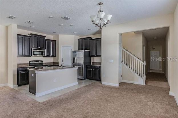 A kitchen with dark cabinets and a granite island opens to a carpeted living area — 13303 PENSHURST LANE, WINDERMERE, FL
