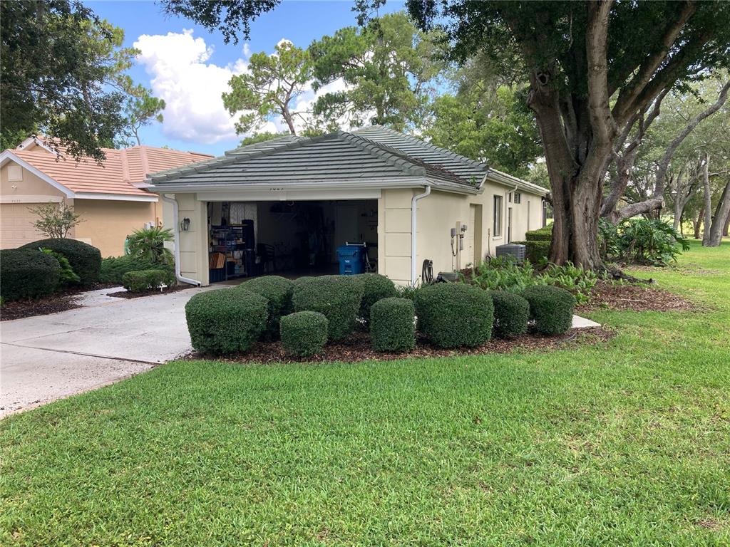 A beige house with a tiled roof, open garage, and manicured shrubs in the front yard — 9029 PENELOPE DRIVE, WEEKI WACHEE, FL