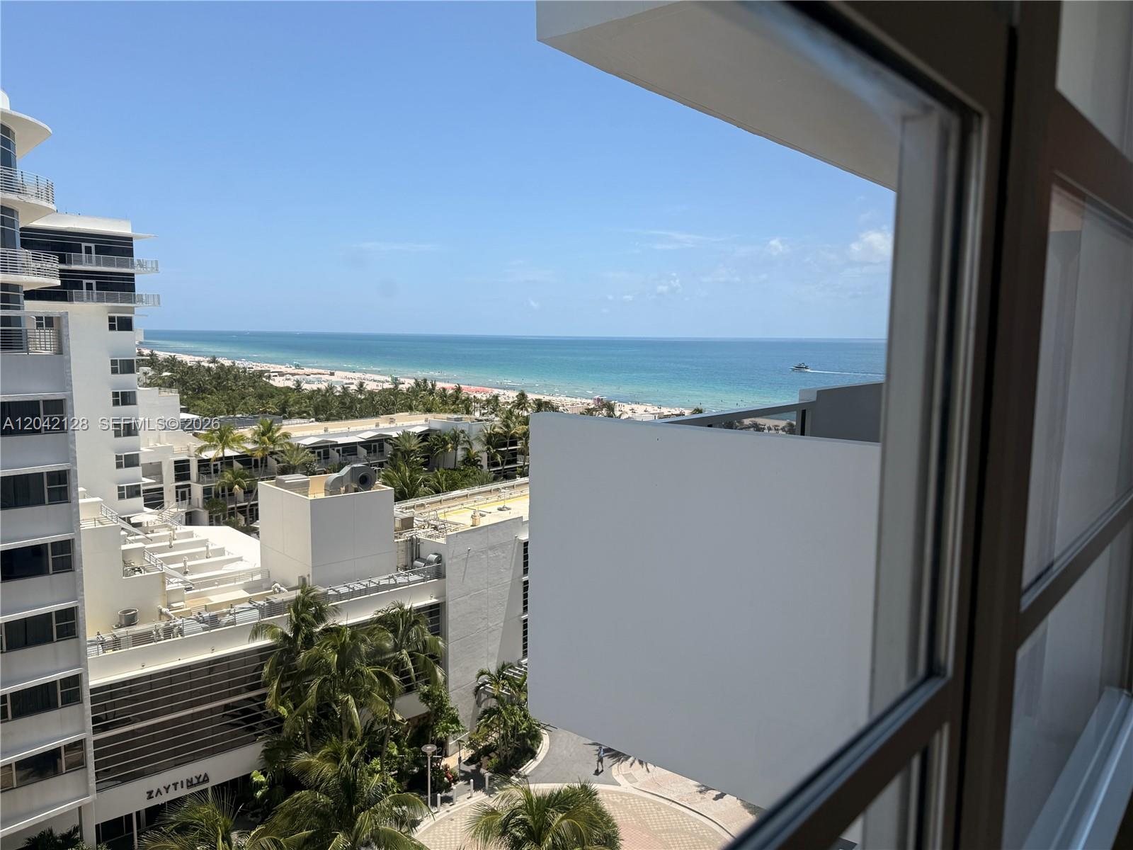 A view from a window overlooking a beach, palm trees, and nearby hotel buildings — 100 Lincoln Rd # 1025, Miami Beach FL 33139, MIAMI BEACH, FL