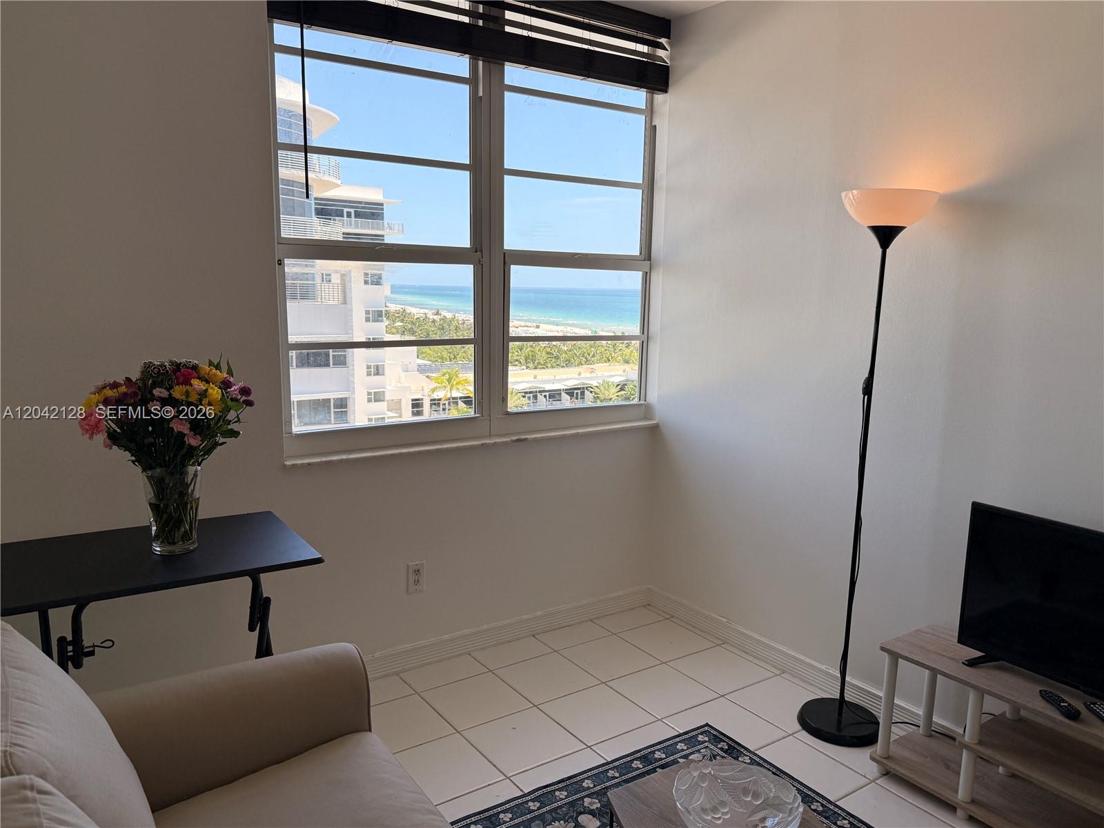 A living room with tile floors, a floor lamp, and a window overlooking the ocean — 100 Lincoln Rd # 1025, Miami Beach FL 33139, MIAMI BEACH, FL