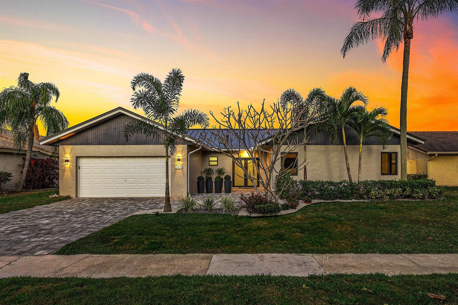 A single-story house with a paved driveway, garage, and palm trees at sunset — 21212 Escondido Way, Boca Raton FL 33433, BOCA RATON, FL