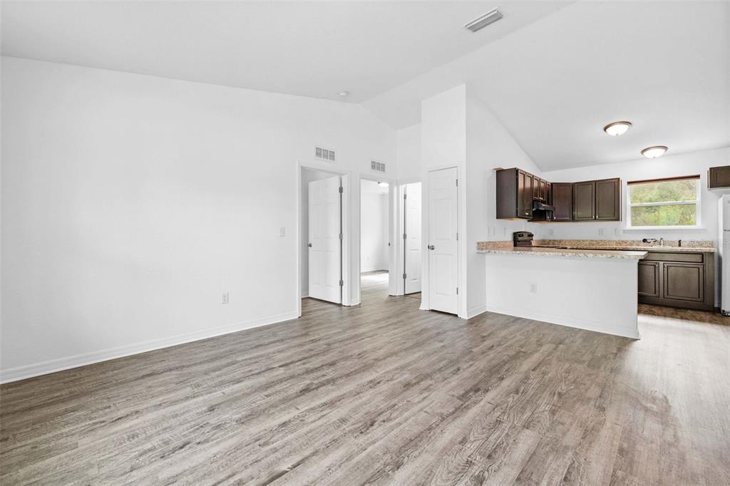 A living room with wood-look flooring leads to an open kitchen with dark wood cabinets — 2549 W CASTANIA DRIVE, CITRUS SPRINGS, FL