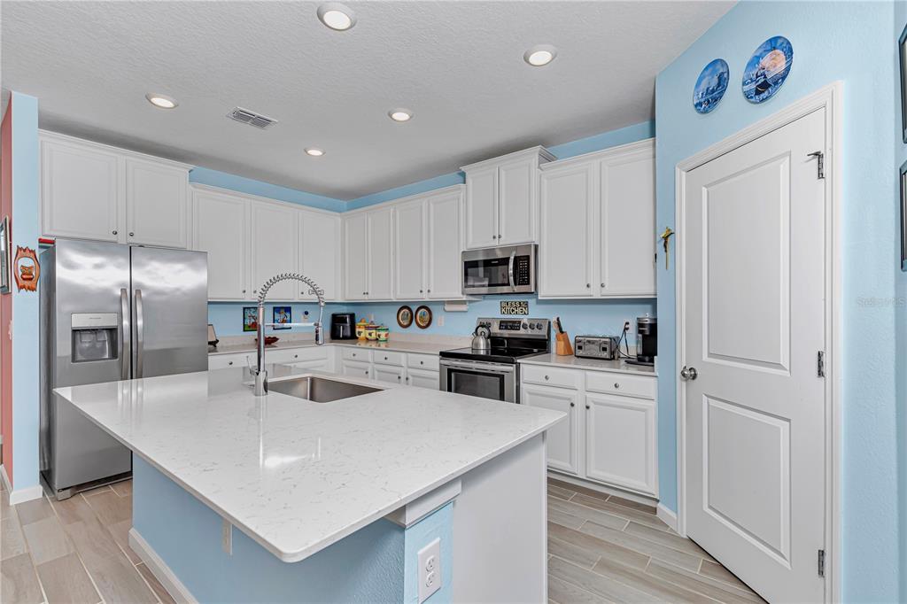 A kitchen features white cabinets, quartz countertops, a center island, and light blue walls — 7509 SW 78TH TERRACE, OCALA, FL