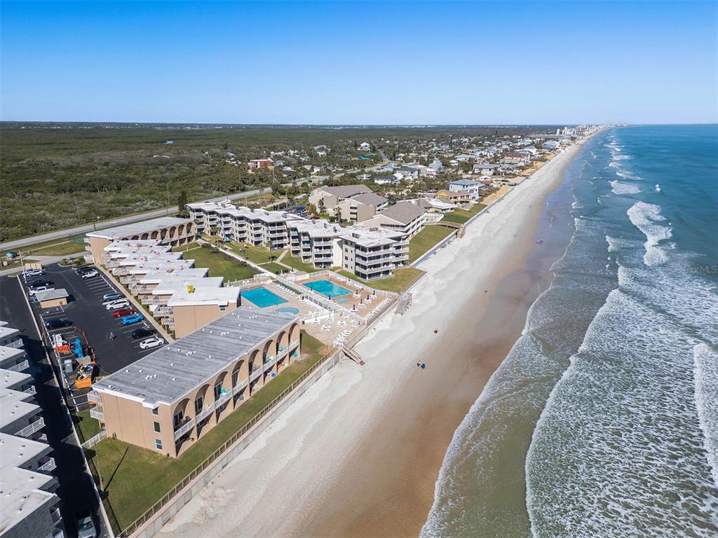 An aerial view shows a beachfront resort complex with multiple buildings, pools, and parking lots — 4821 SAXON DRIVE UNIT B-213, NEW SMYRNA BEACH, FL