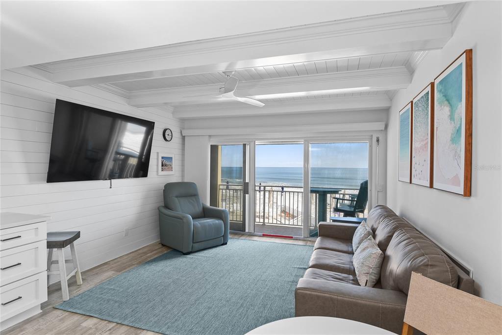 A living room with white shiplap walls, a leather sofa, and a view of the ocean — 4821 SAXON DRIVE UNIT B-213, NEW SMYRNA BEACH, FL