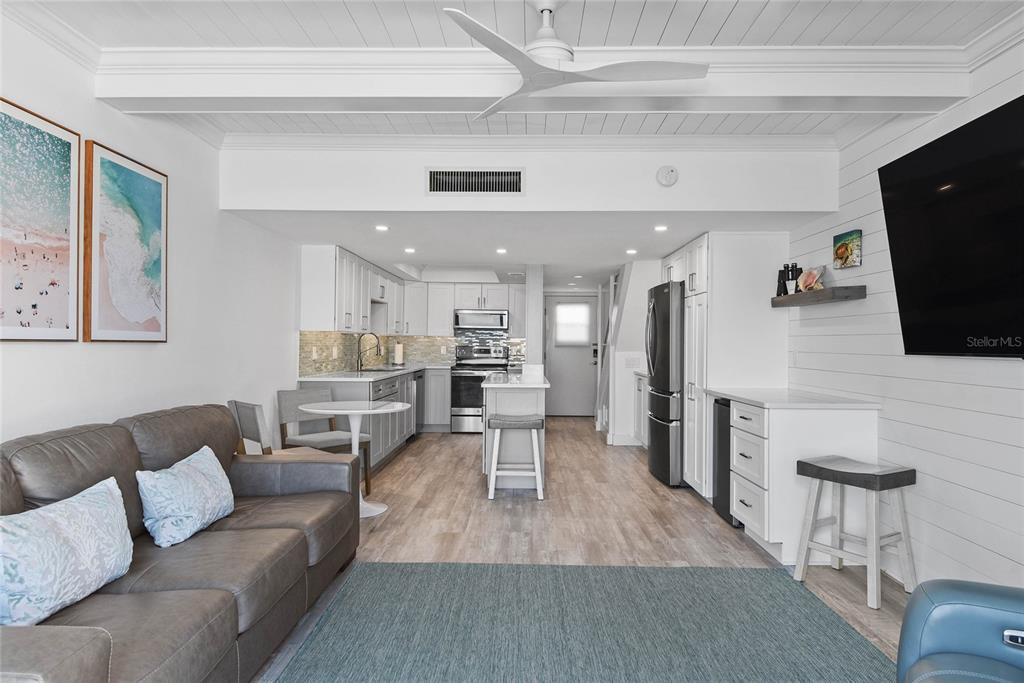 A bright, open-concept living room and kitchen area features white cabinetry and wood-look flooring — 4821 SAXON DRIVE UNIT B-213, NEW SMYRNA BEACH, FL