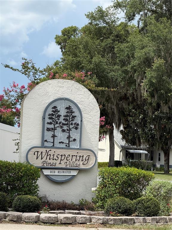 A sign for Whispering Pines Villas stands in front of trees and a residential building — 517 WHISPERING PINES BOULEVARD, INVERNESS, FL