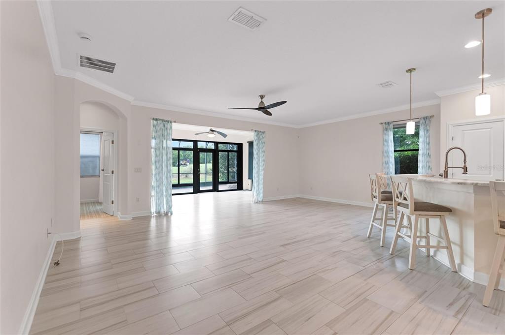 An open-concept living area features light wood-look tile floors, a kitchen island, and sliding doors — 8972 DOVE VALLEY WAY, DAVENPORT, FL