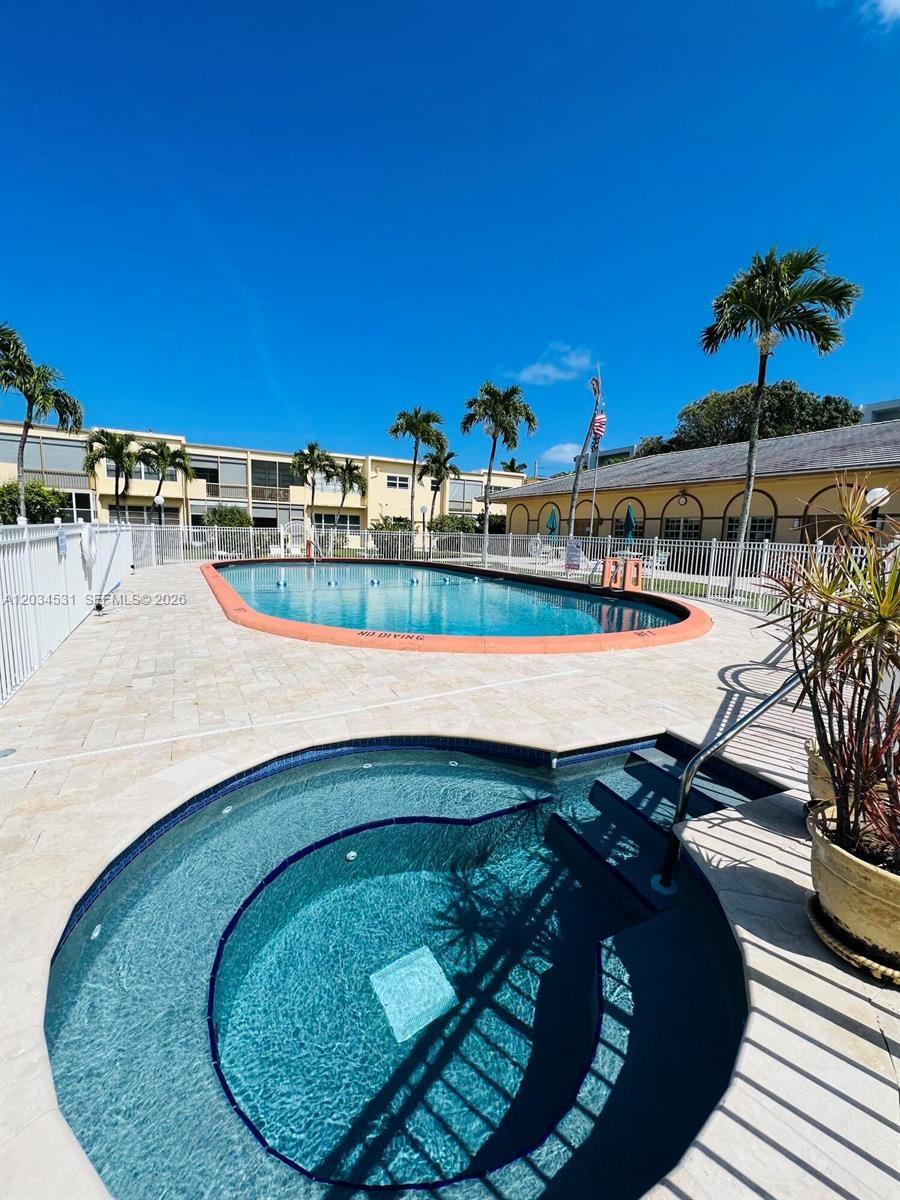A swimming pool and a circular hot tub are situated on a paved pool deck — 851 NE 14th Ave # 414, Hallandale Beach FL 33009, HALLANDALE BEACH, FL