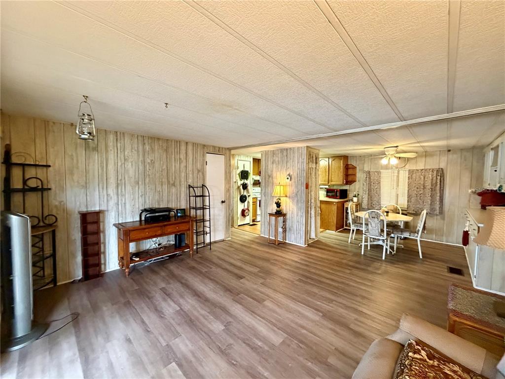 A living room with wood-look flooring and wood-paneled walls opens into a dining area and kitchen — 5301 ALGERIA COURT, BRADENTON, FL