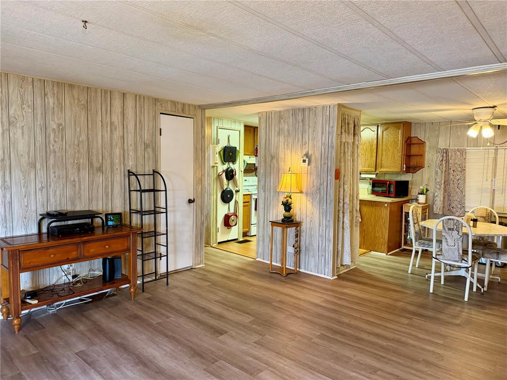 A living room with wood-paneled walls and vinyl flooring opens into a kitchen and dining area — 5301 ALGERIA COURT, BRADENTON, FL