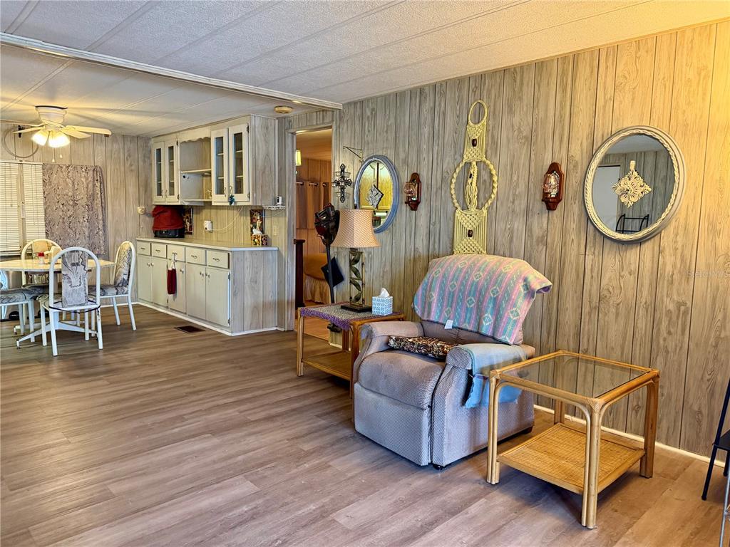 A living room with wood-paneled walls, a recliner, and an adjacent kitchen area — 5301 ALGERIA COURT, BRADENTON, FL