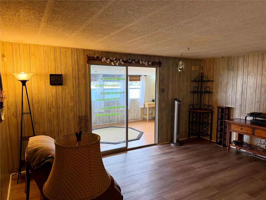 A living room features wood-paneled walls, wood-look flooring, and a sliding glass door to a sunroom — 5301 ALGERIA COURT, BRADENTON, FL