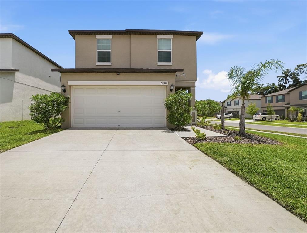 A two-story suburban house features a beige stucco exterior, a two-car garage, and a driveway — 6298 BAR S BAR TRAIL, ZEPHYRHILLS, FL