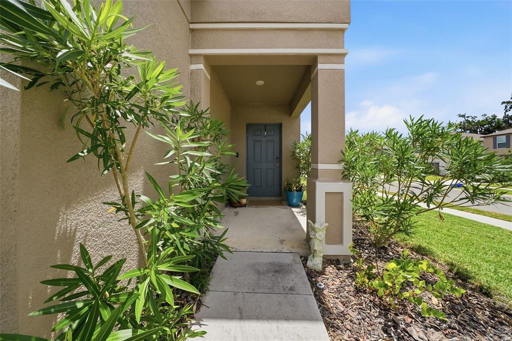 A concrete walkway leads to the covered front entrance of a tan stucco home — 6298 BAR S BAR TRAIL, ZEPHYRHILLS, FL