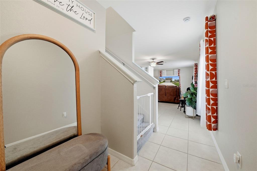 A hallway with a mirror, a staircase with a baby gate, and tile flooring — 6298 BAR S BAR TRAIL, ZEPHYRHILLS, FL