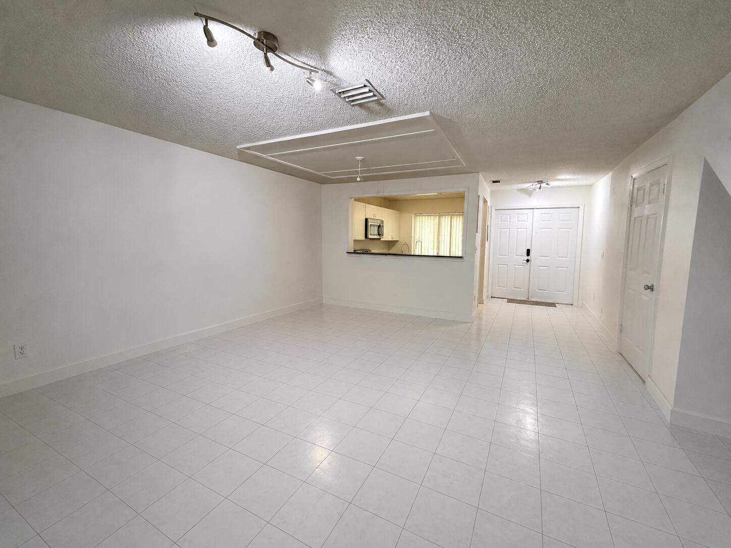 An open-concept living area features white tile flooring, white walls, and a kitchen pass-through window — 12272 NW 36th Place, Sunrise FL 33323, SUNRISE, FL