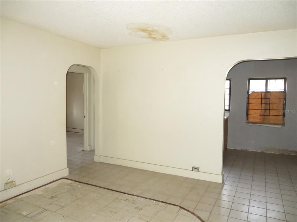 An interior view of a room with tiled floors, arched doorways, and a water-stained ceiling — 420 W CHERRY STREET, KISSIMMEE, FL