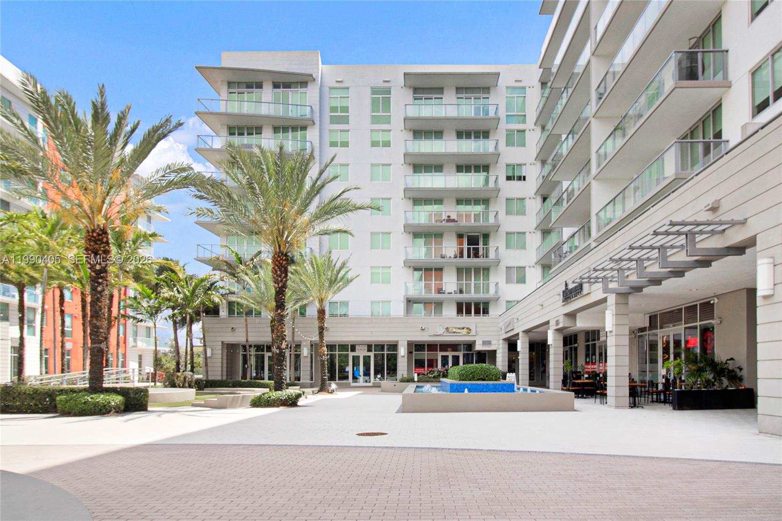 A modern multi-story apartment building features balconies, palm trees, and a ground-level courtyard fountain — 7661 NW 107th Ave # 501, Doral FL 33178, DORAL, FL