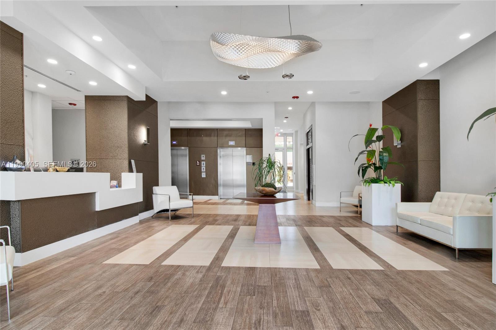 A modern building lobby features a reception desk, white seating, elevators, and a textured chandelier — 7661 NW 107th Ave # 501, Doral FL 33178, DORAL, FL